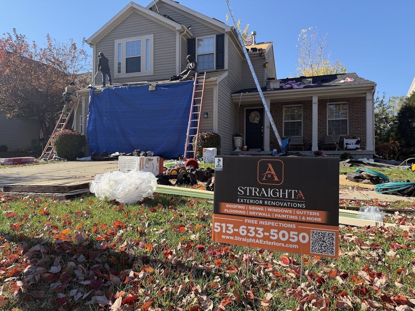 Roof tear-off in progress with blue tarps spread over the ground to catch debris